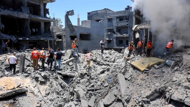 Rescatistas y civiles sobre los escombros de un edificio destruido durante un bombardeo israelí sobre el campo de refugiados de Al Shati.
