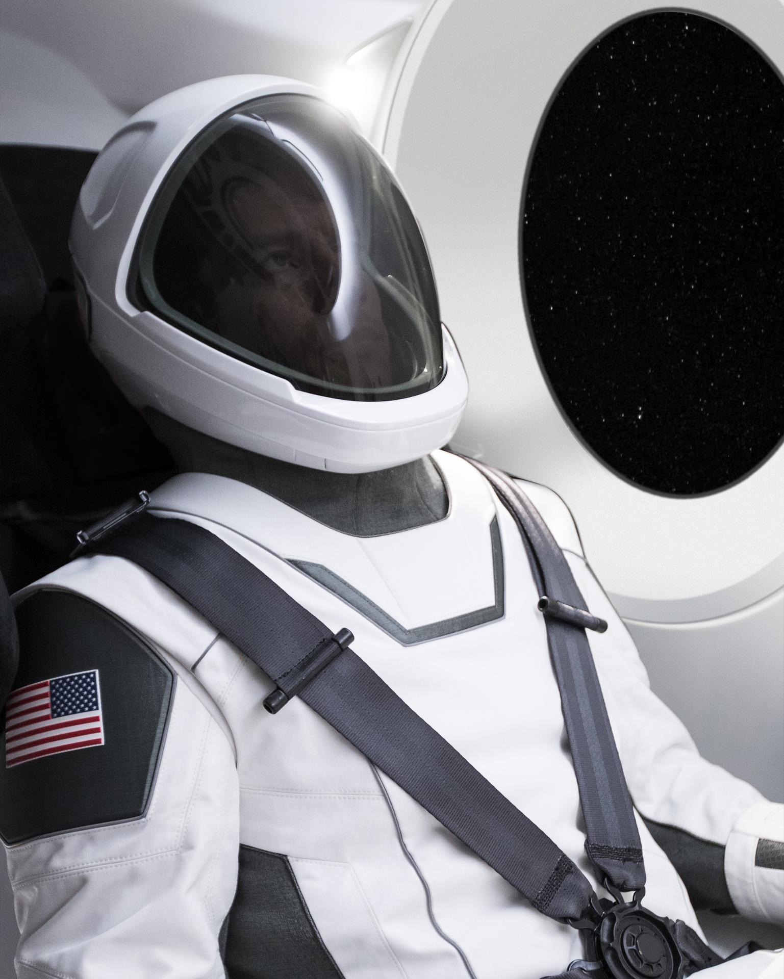 A man in a white spacesuit sitting in the capsule of the SpaceX Dragon Crew Module.