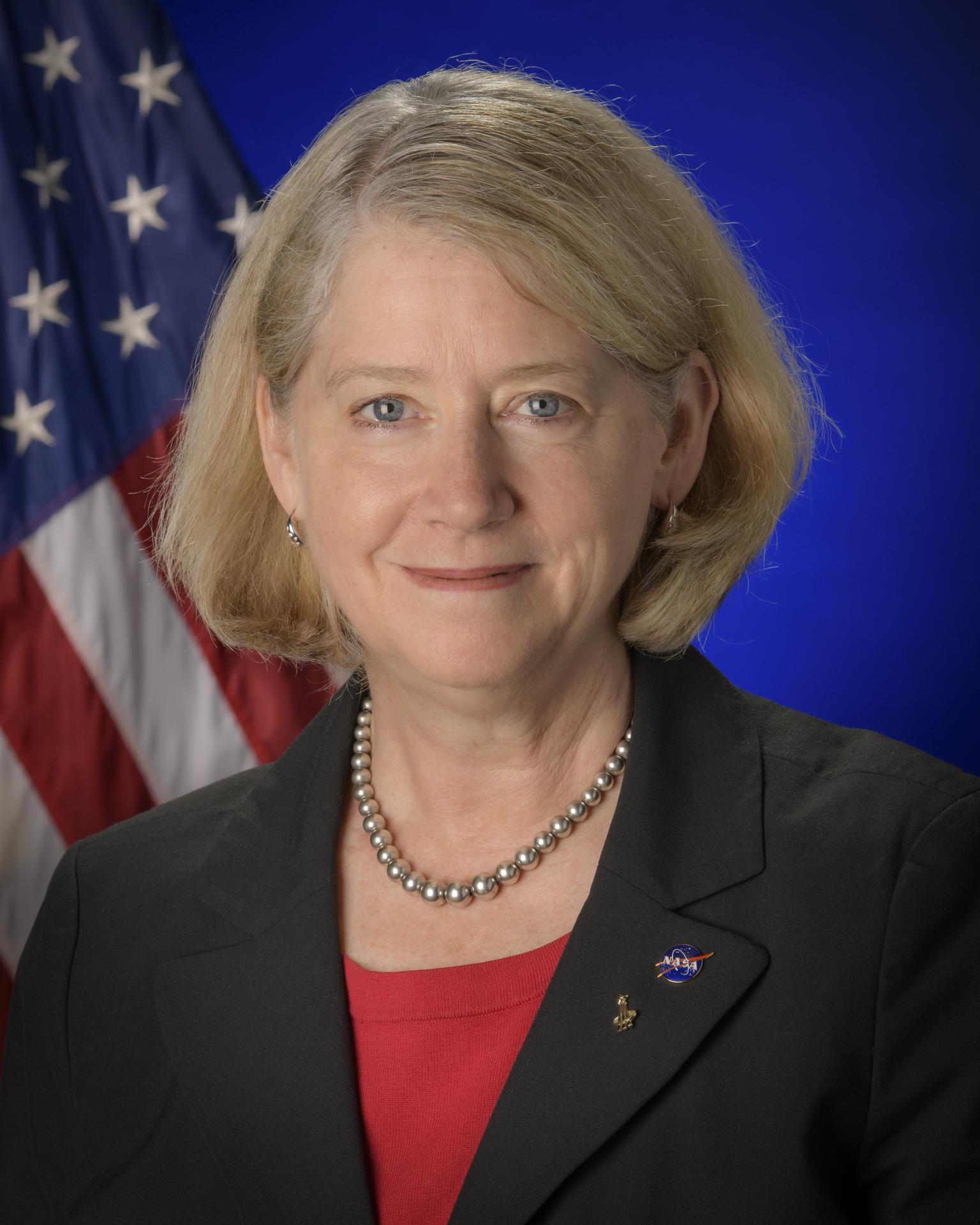 Deputy Adminstrator Pam Melroy in a blue suit with a red top and the American flag in the backgroud.