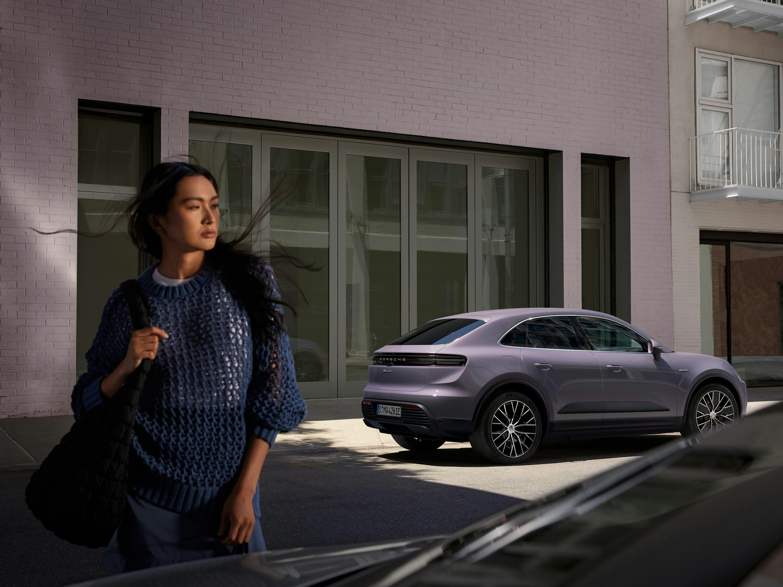 A woman walks in front of a Macan on a city street.