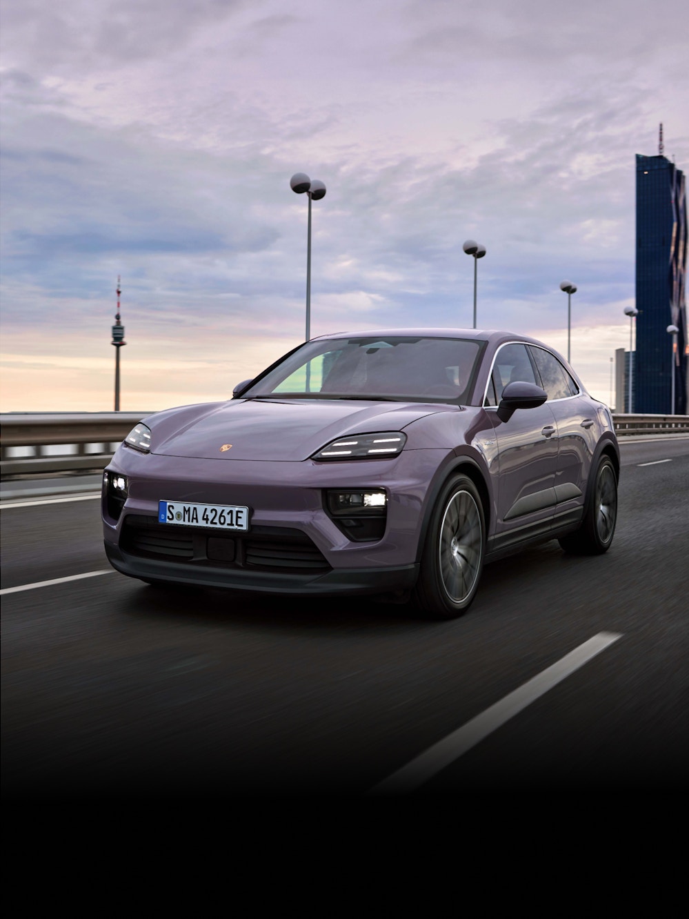 A Porsche all-electric Macan driving down a road in an urban scenario.