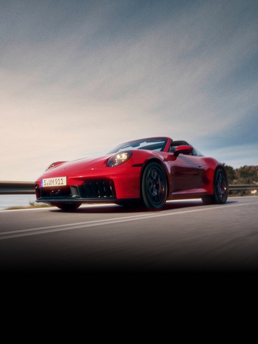 A red Porsche 911 driving down a road with nature in the background. 