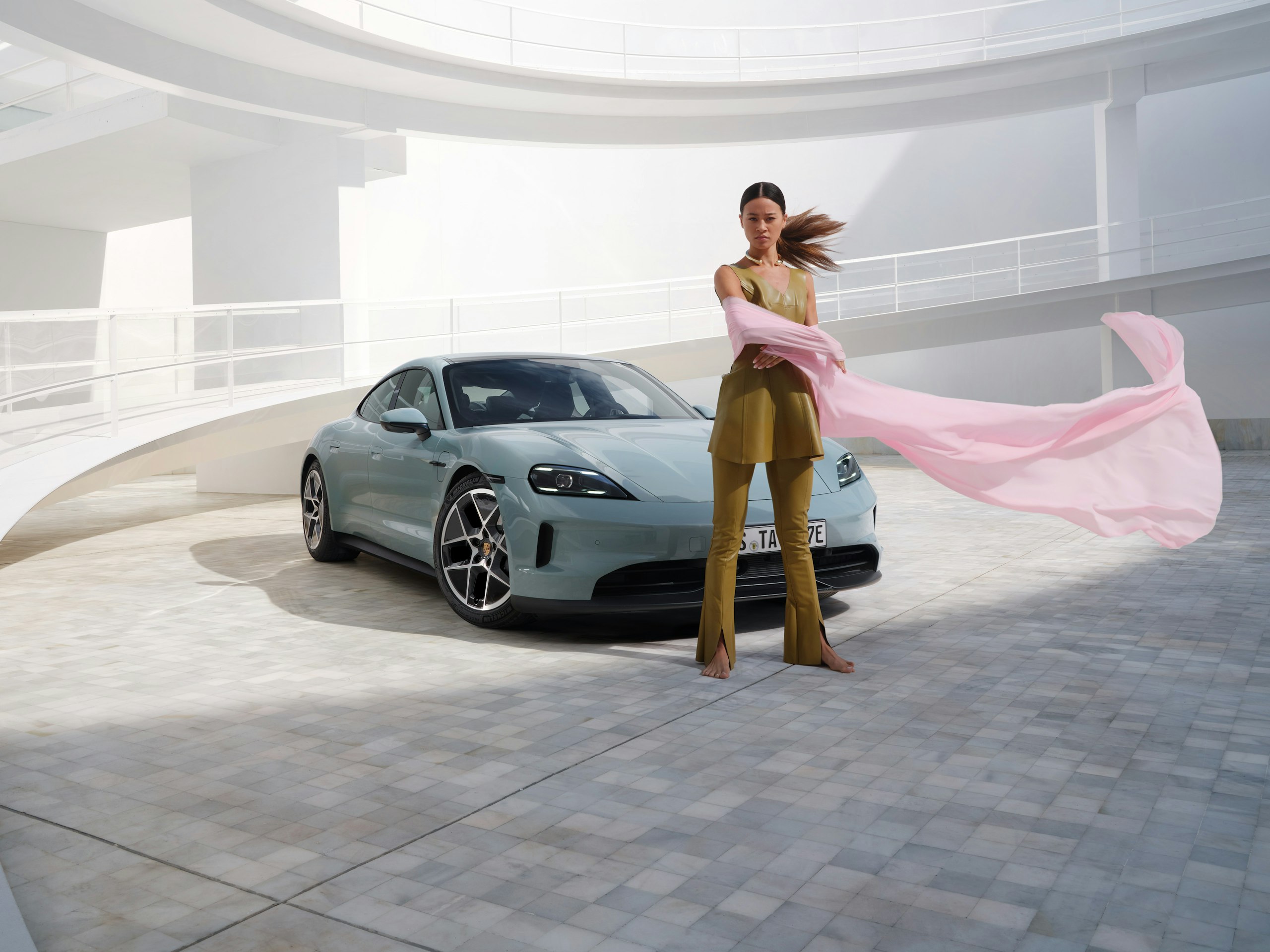 A woman standing in front of a shadegreen metallic Taycan in a modern setting.