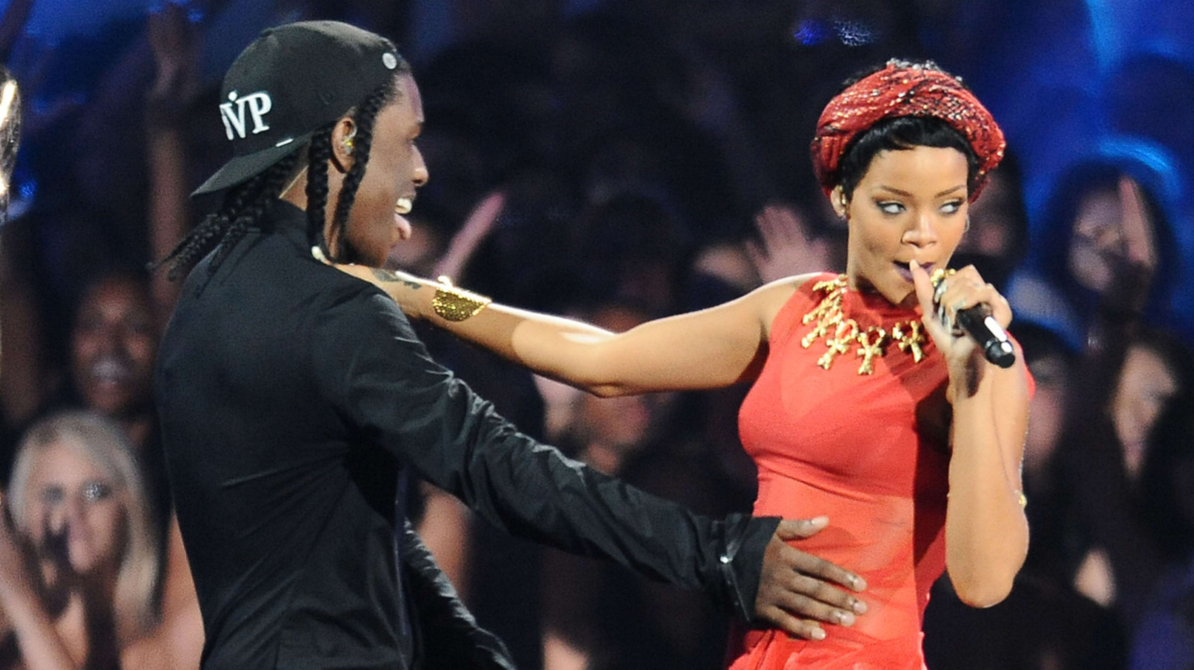 Two performers on stage; Rihanna in red with a headset mic, ASAP Rocky in black with cap, engaging with the audience