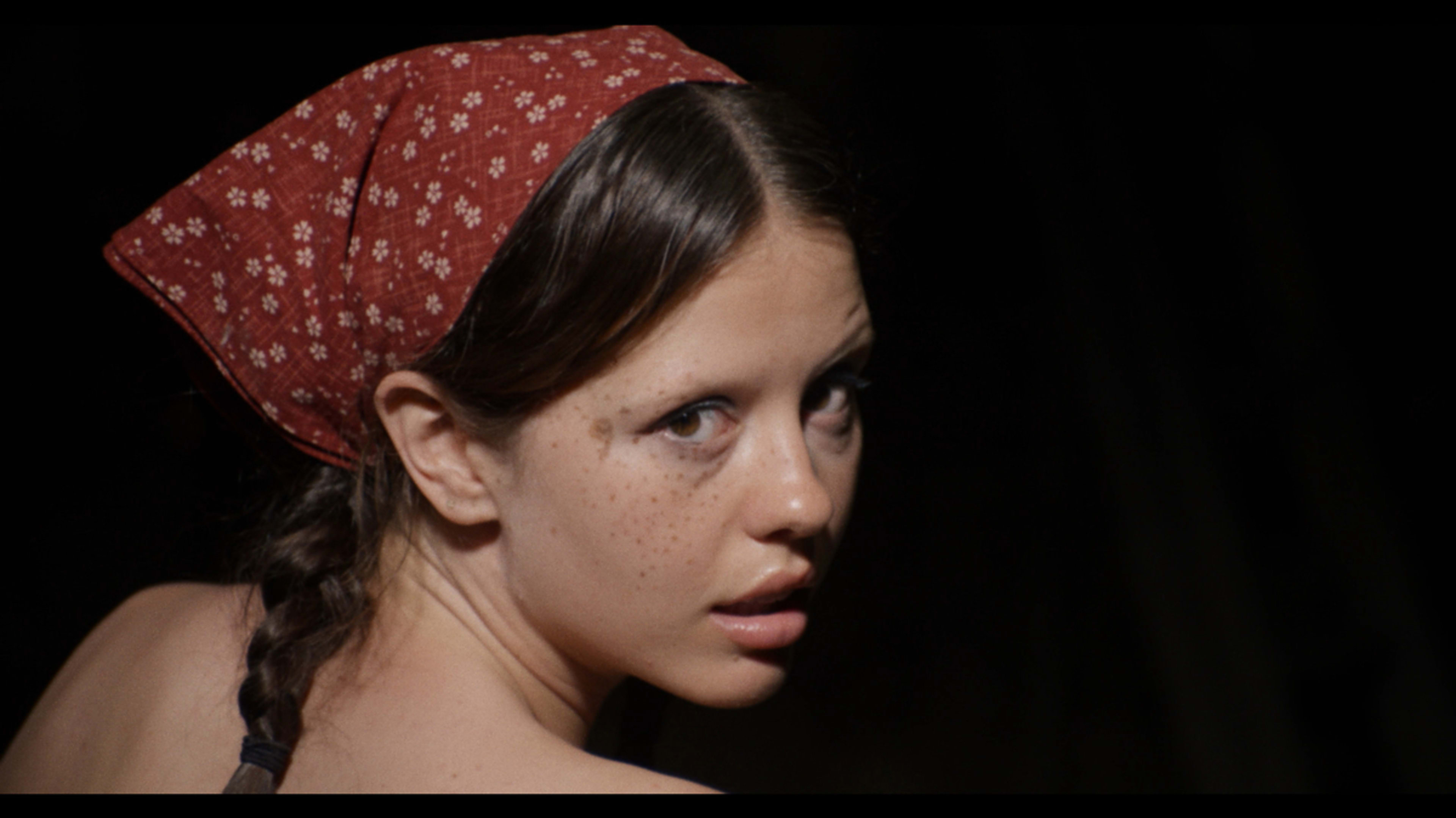 Woman with a red headscarf and braid looks over her shoulder with a surprised expression