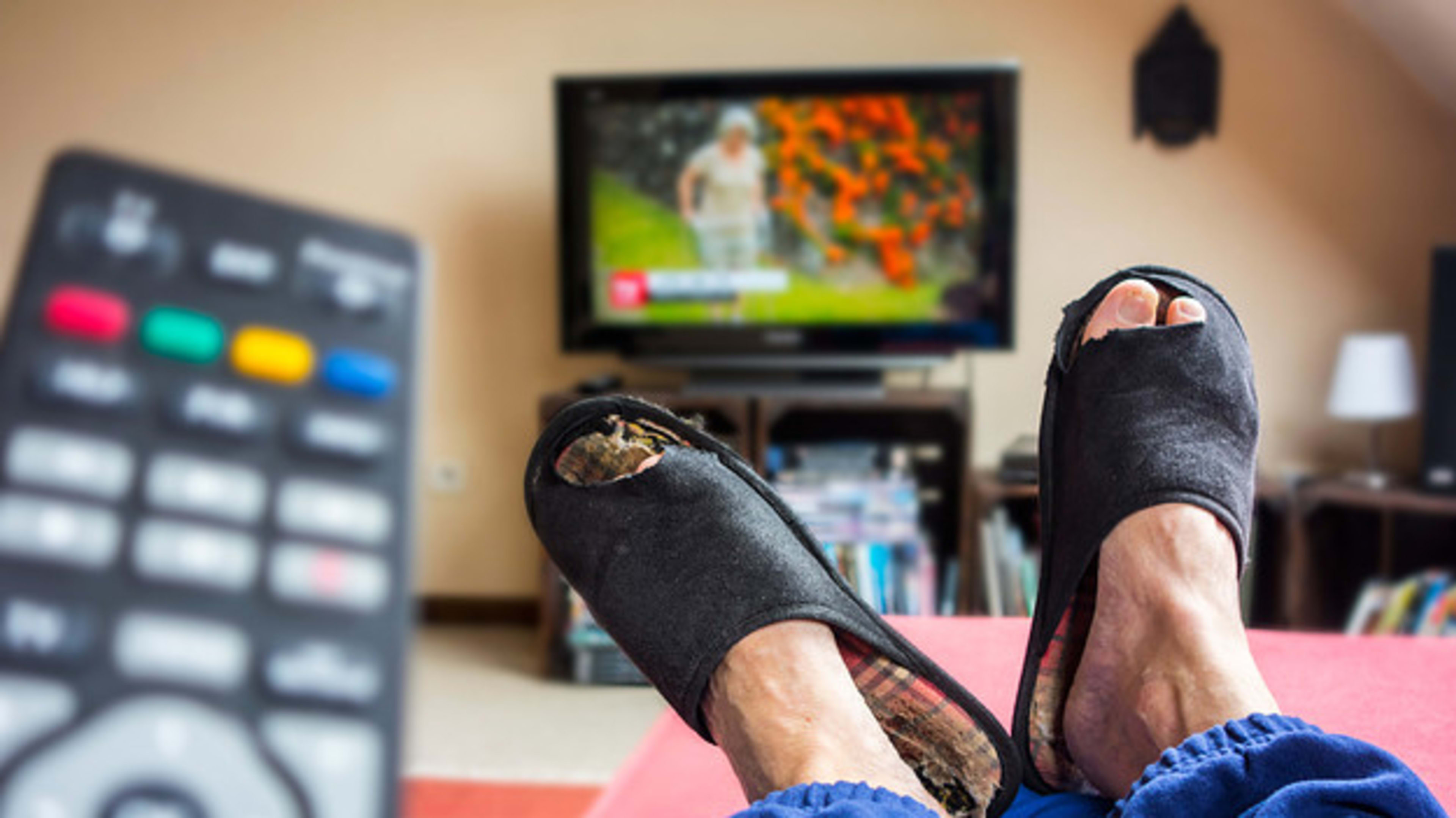 Remote control and couch potato, lazy man in comfy chair wearing worn slippers