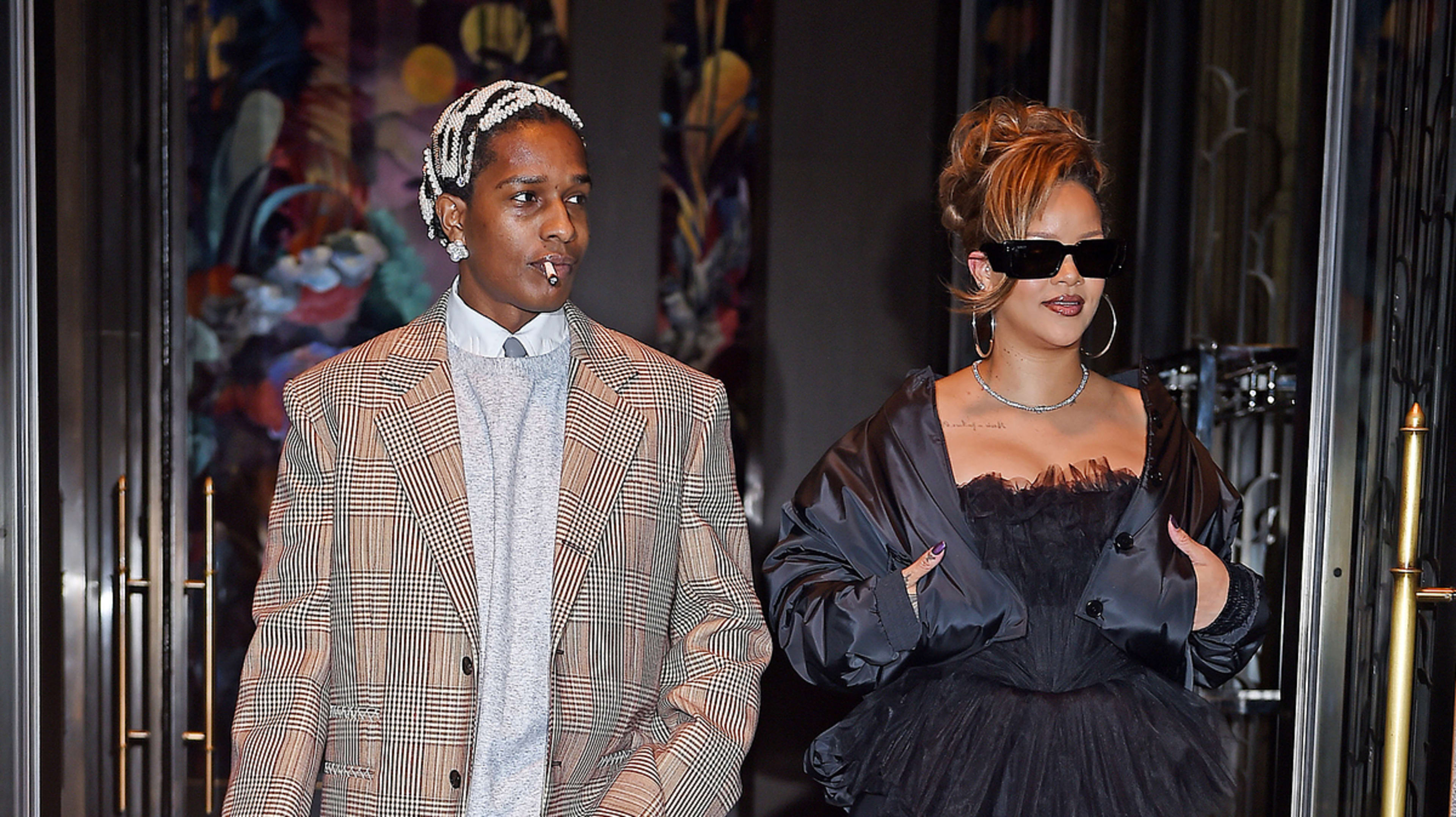 Two individuals, one in a pinstripe suit and the other in a voluminous dress, walking out of a building