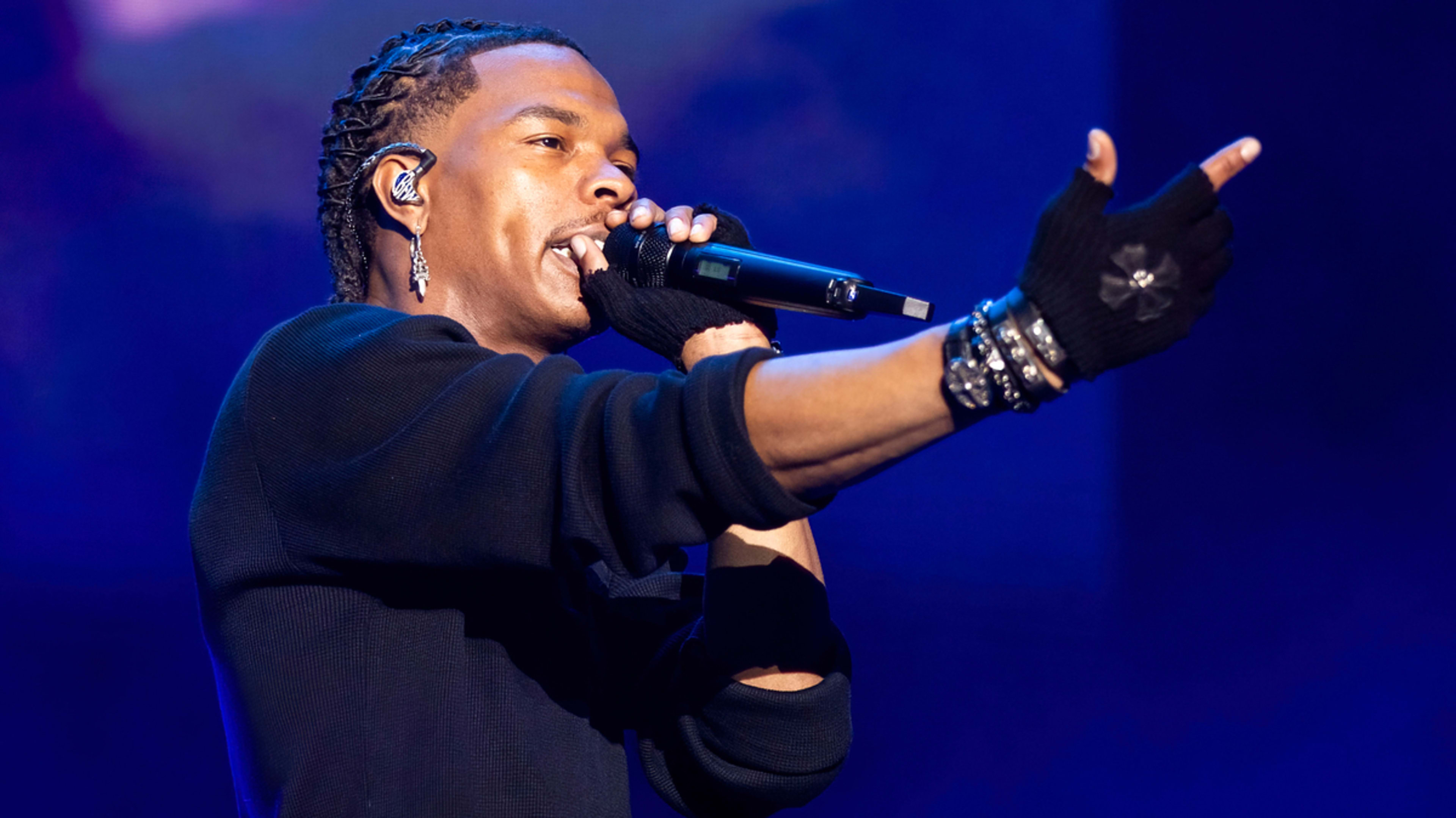 Lil Baby performing on stage, holding a microphone, wearing black gloves and an earring