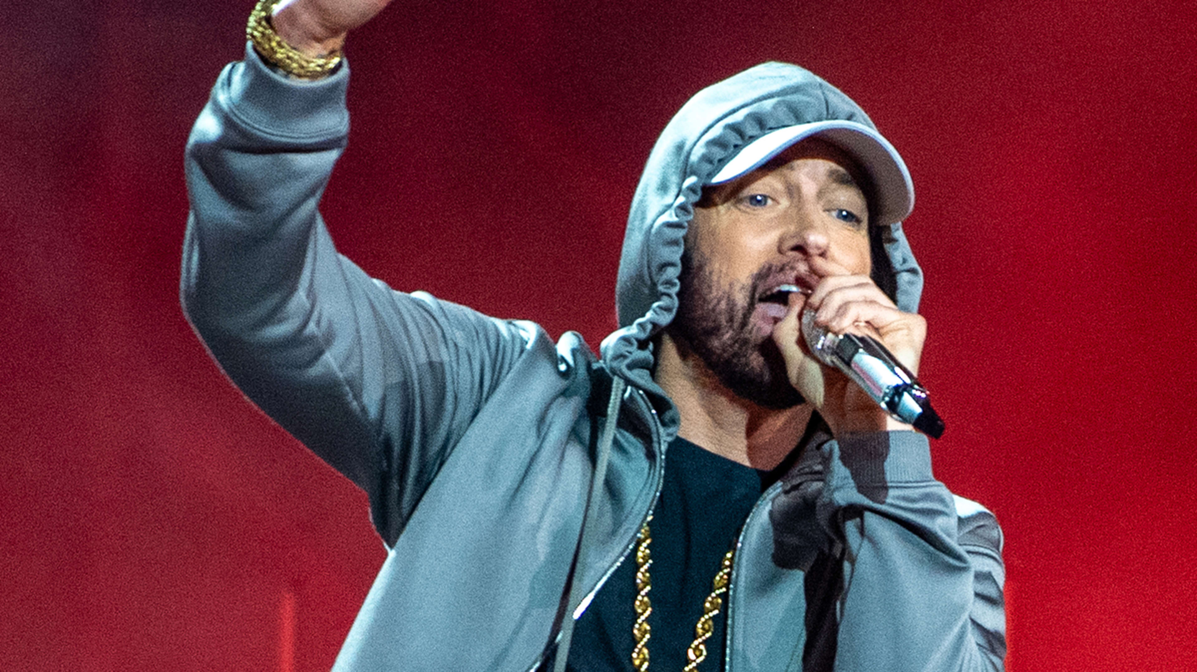 Eminem performs on stage wearing a grey hoodie, gold chain, and holding a microphone