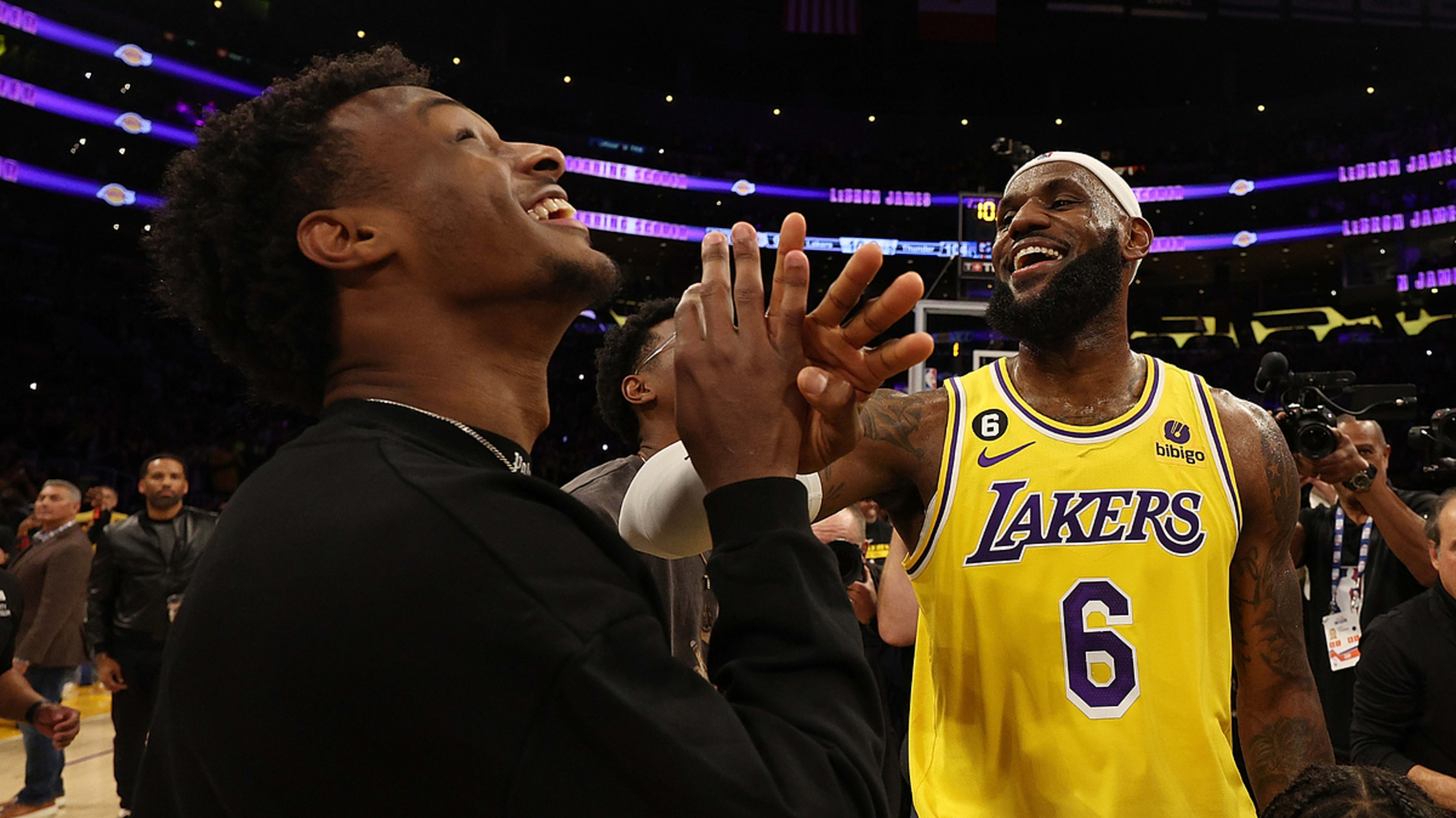 LeBron James in a Lakers jersey and his son Bronny James share a joyful moment on a basketball court, laughing and clasping hands