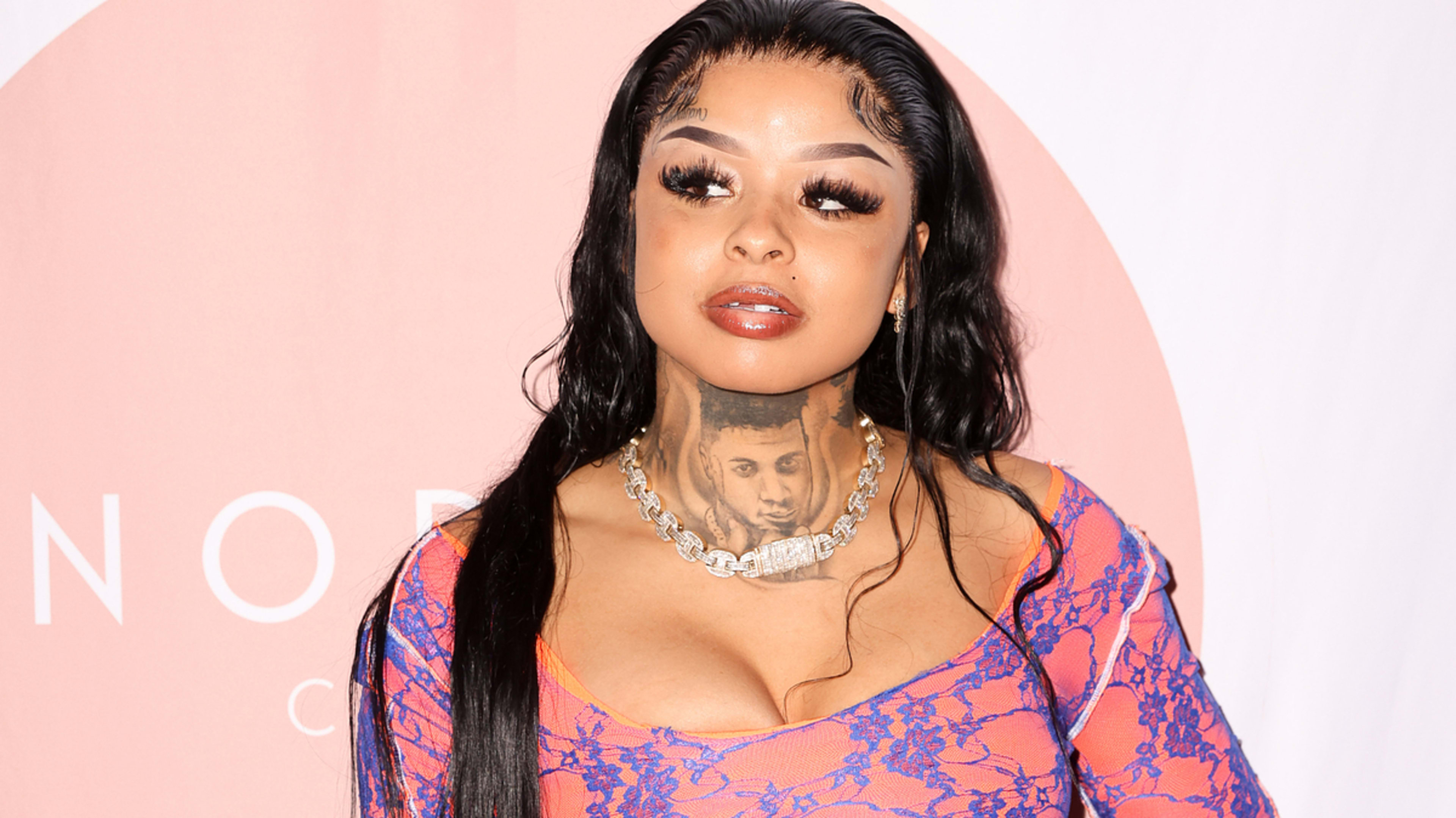 The image shows Chrisean Rock posing on the red carpet in a lace-patterned dress, showing her diamond necklace and tattoo on her neck