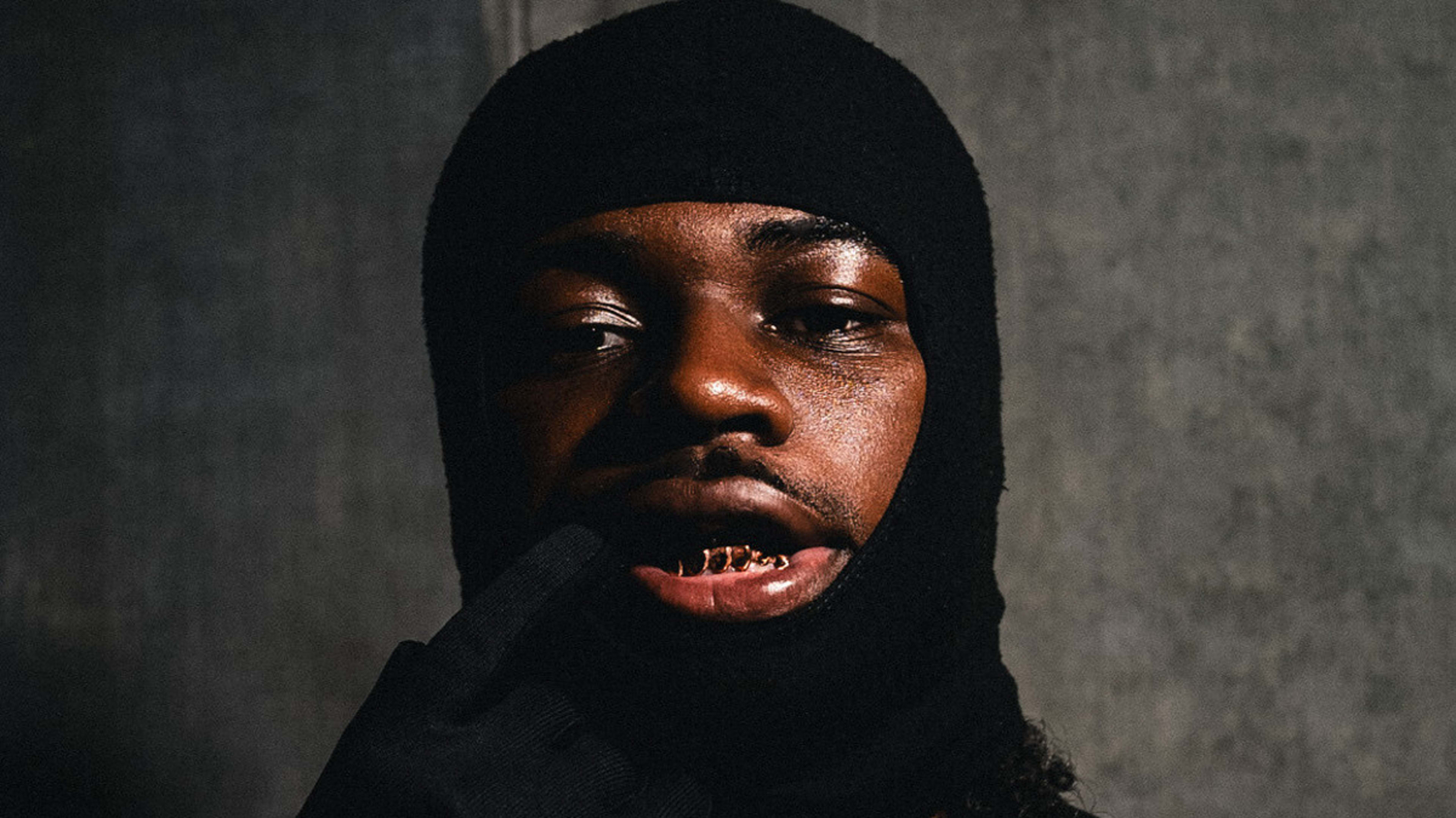 Person in a black sleeveless top and ski mask, wearing a glove, posing thoughtfully