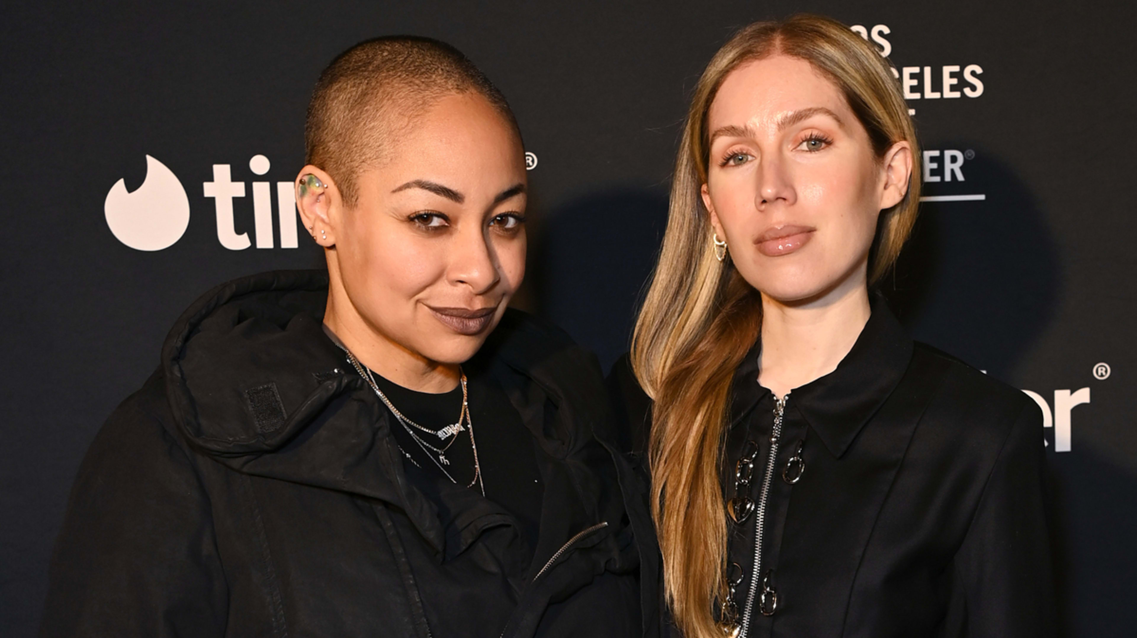 Two individuals posing together at an event, one in a black jacket and the other in an embellished black top