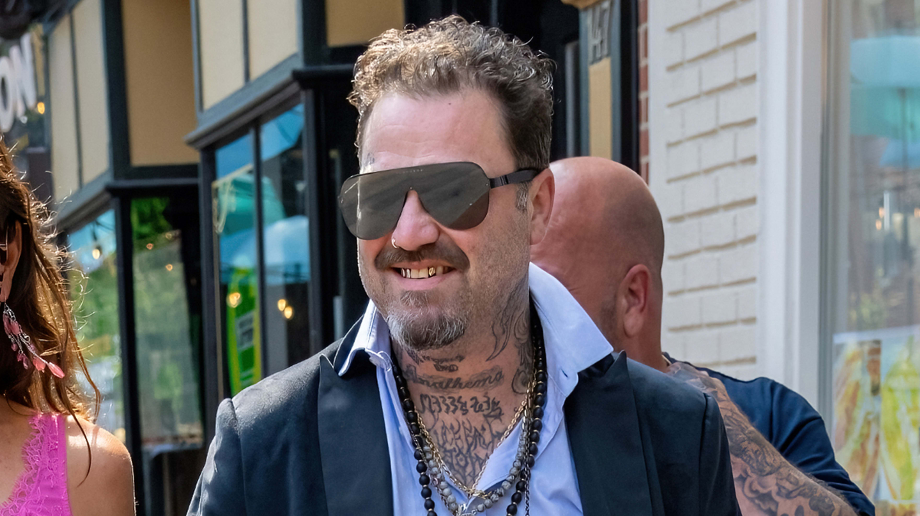 Bam Margera in sunglasses and tattooed, wearing a casual black outfit, walking outside