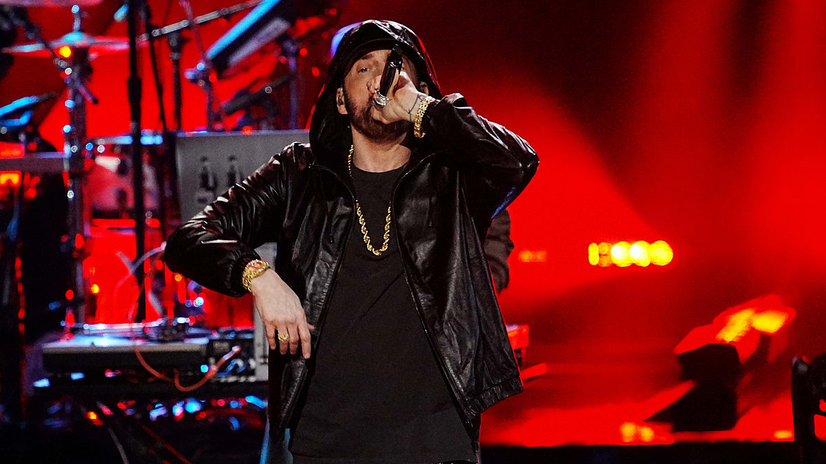 Eminem performs on stage, wearing a leather jacket and holding a microphone