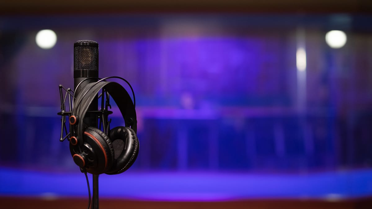 Studio microphone with headphones hanging on it, background blurred with purple hue. No persons visible