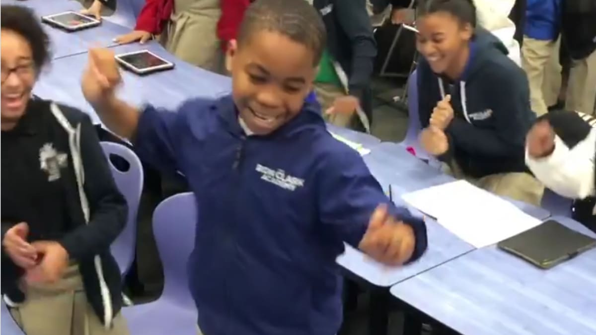 Children in a classroom excitedly dancing and laughing together, some with tablets on desks