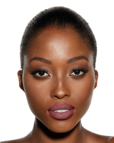 A dark-tone, brunette model with flawless skin wearing a matte, nude-pink lipstick with dark, smokey eyes.