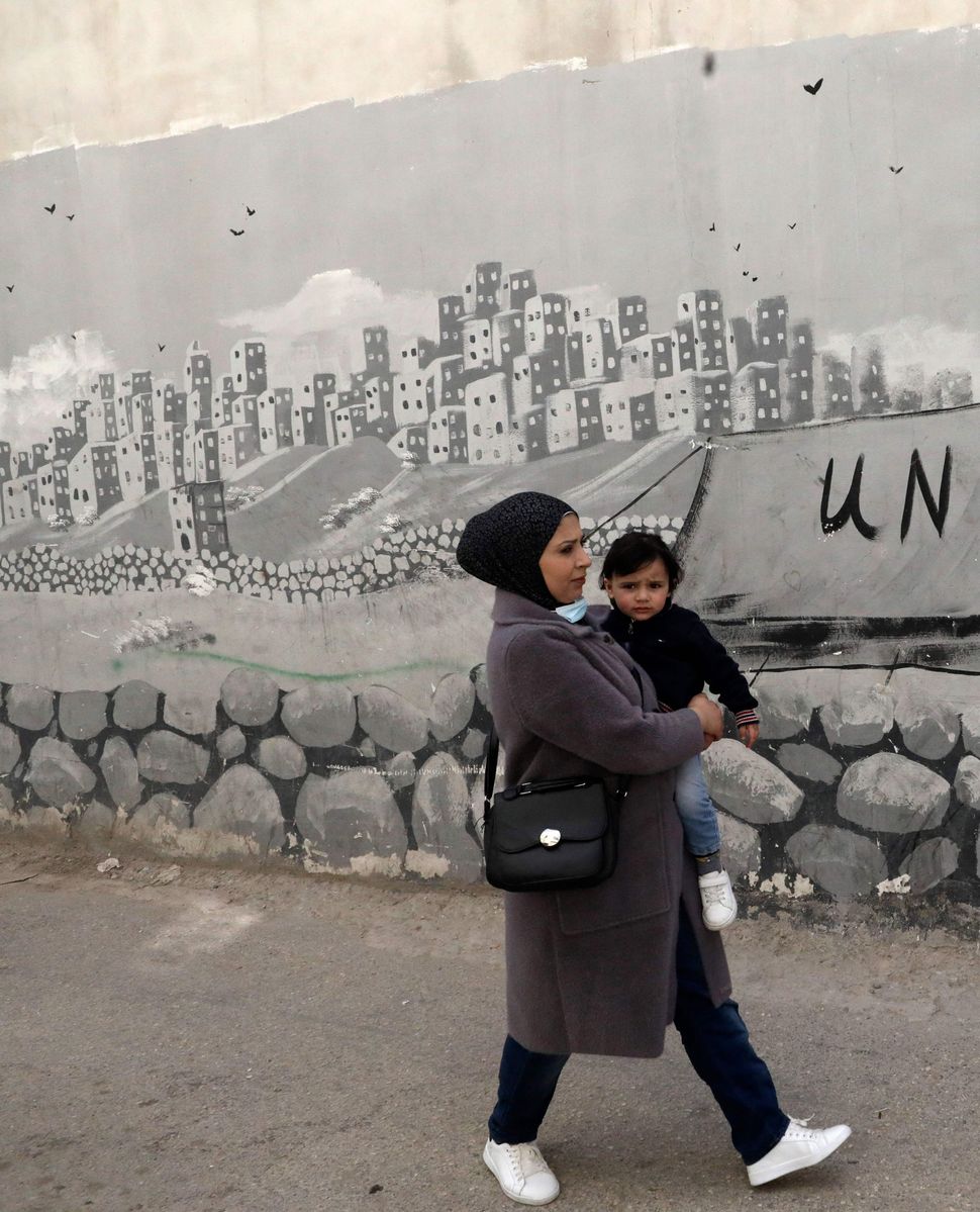 Woman carries child in West Bank refugee camp