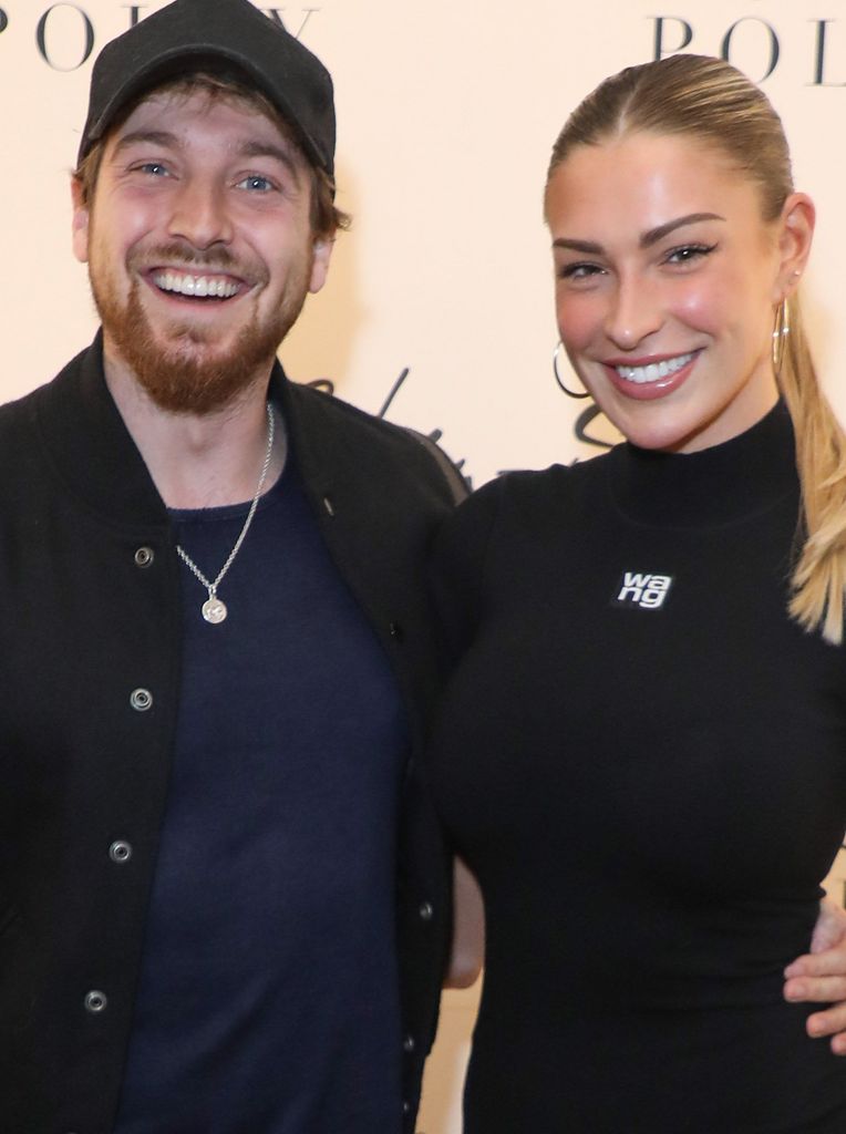 Sam Thompson and Zara McDermott smiles as they pose in front of branding for fashion event