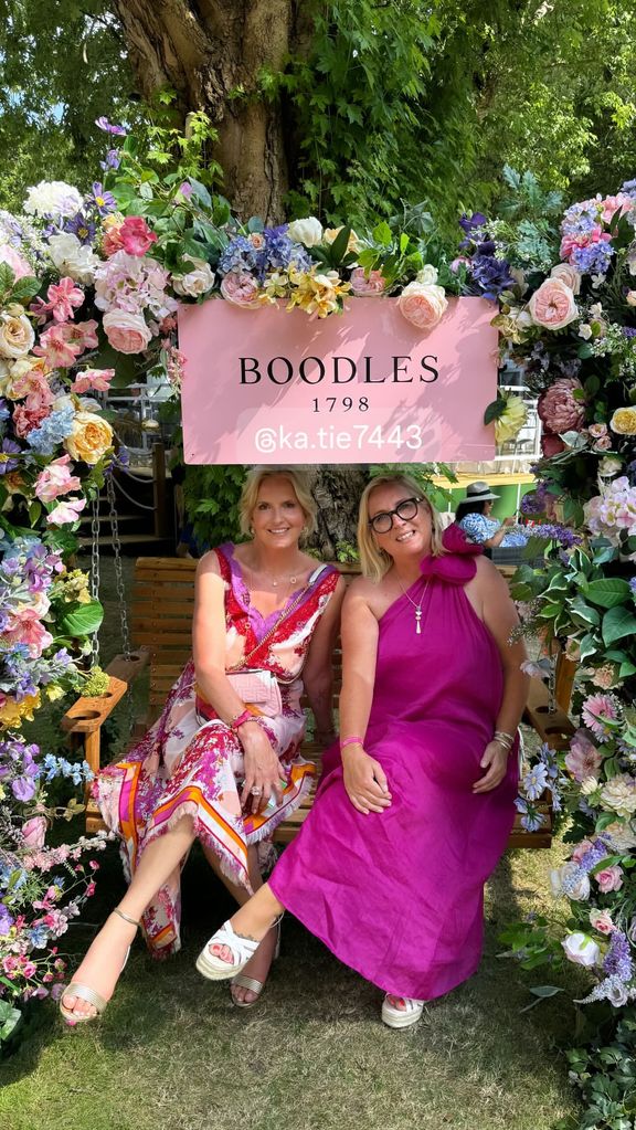 Penny Lancaster in a pink and red dress sitting under a floral arch