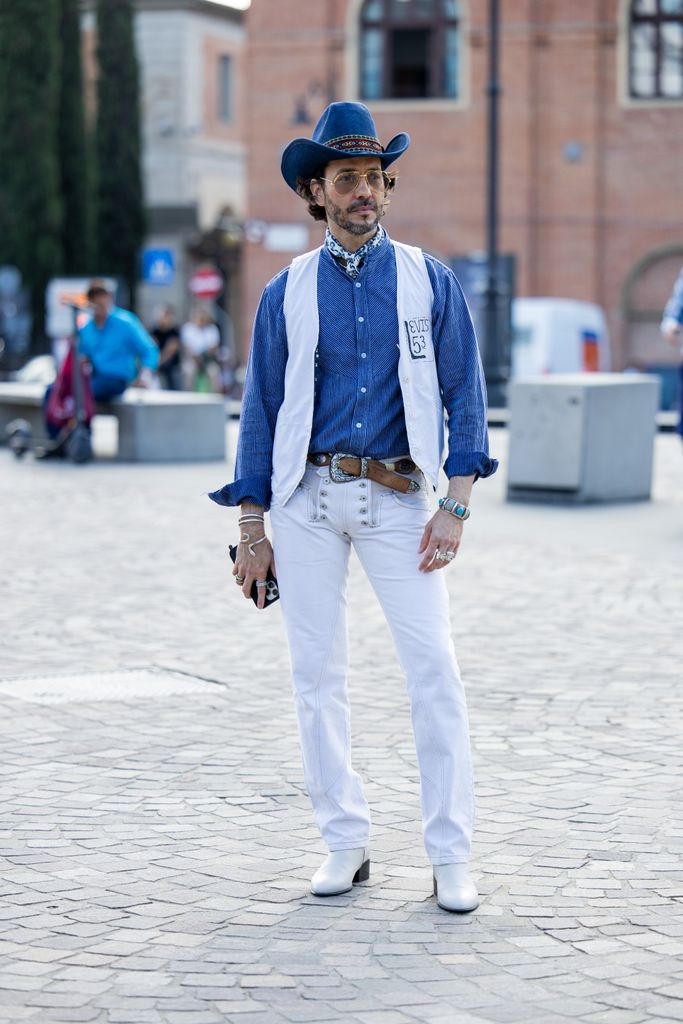 A guest wears blue cowboy hat, vest, denim button shirt, white pants during Pitti Immagine Uomo 106