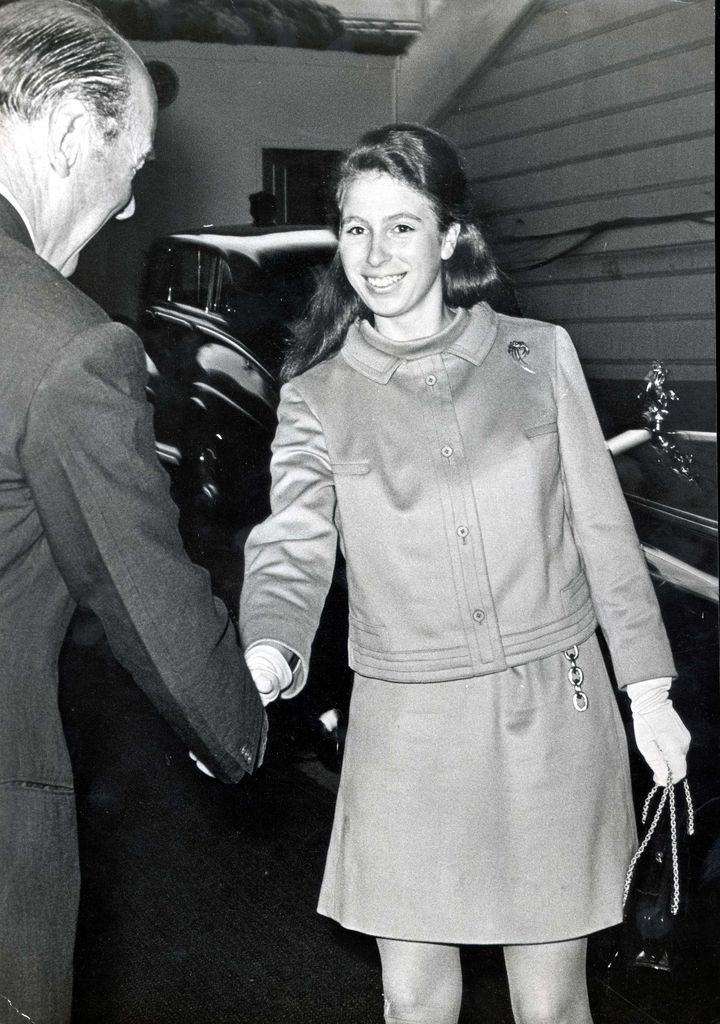 Princess Anne shakes hands with a man. She is wearing a mini skirt and cropped jacket with her hair down