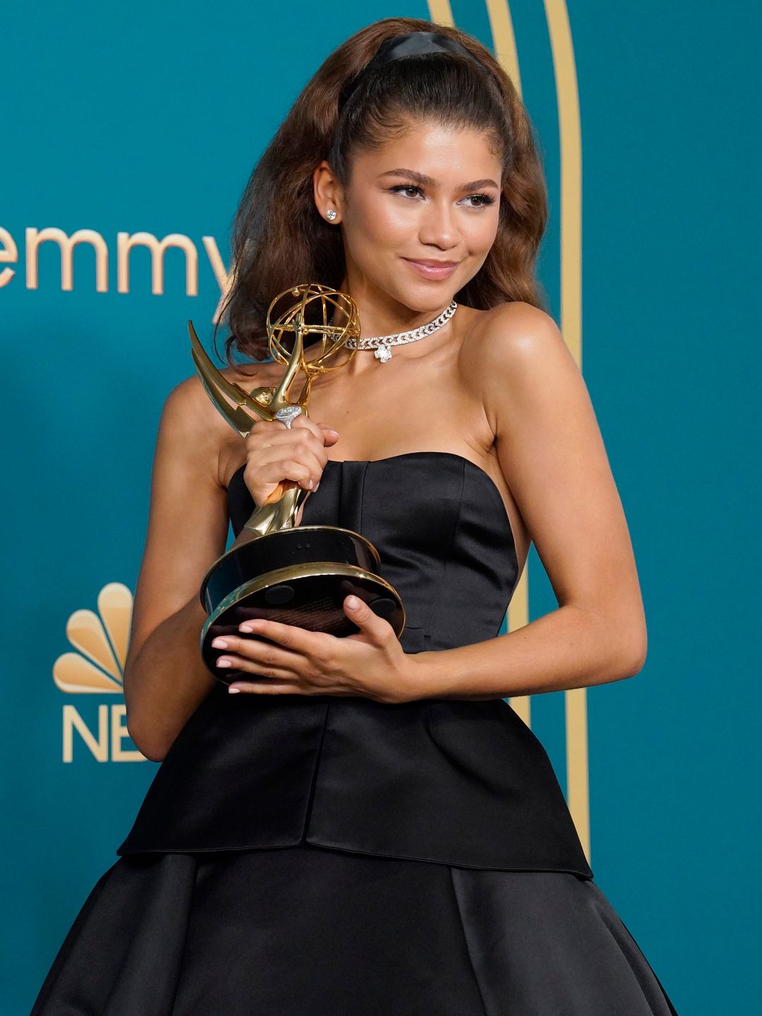 Zendaya smiling on a red carpet holding an emmy