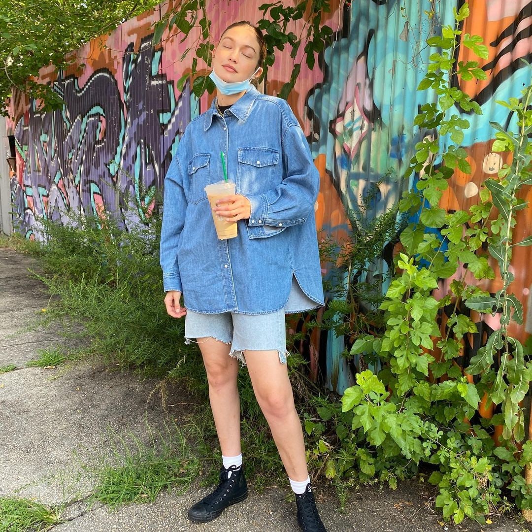 Gigi Hadid wears denim shorts and a denim shirt while holding an ice coffee