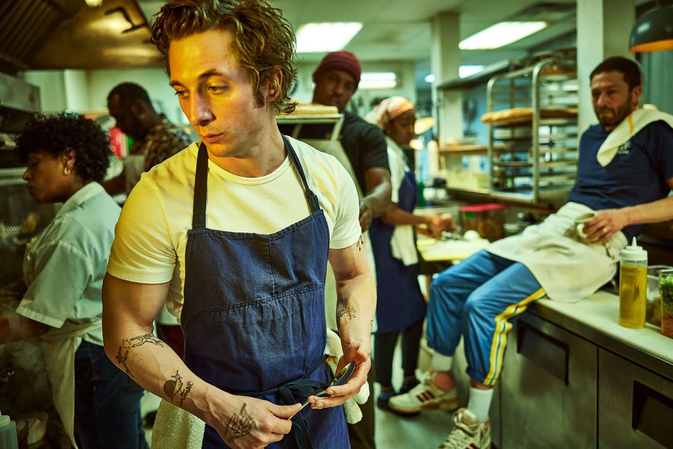 Carmen standing in the kitchen while his staff are cooking and working in the behind him