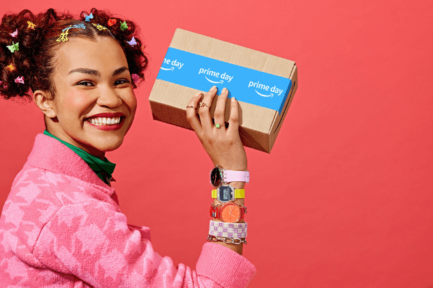 A woman in a pink jacket holding an Amazon package and smiling