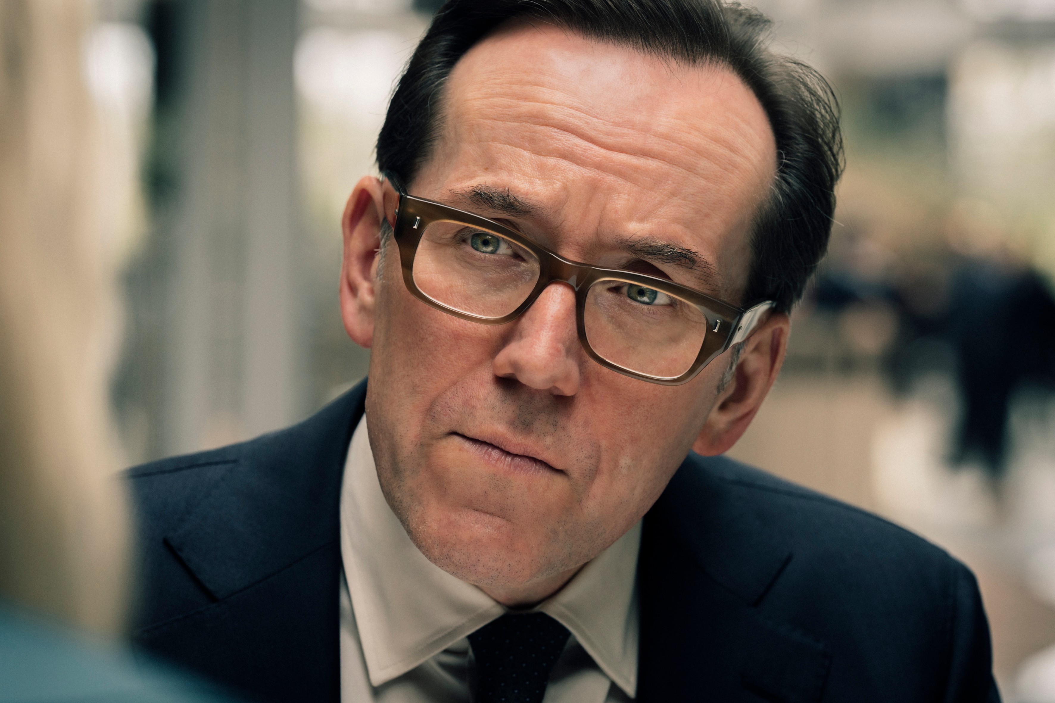 Ben Miller as Detective Superintendent Richard Grove in Suspect season 2 sitting across the table from someone and listening to them, wearing glasses and a suit.