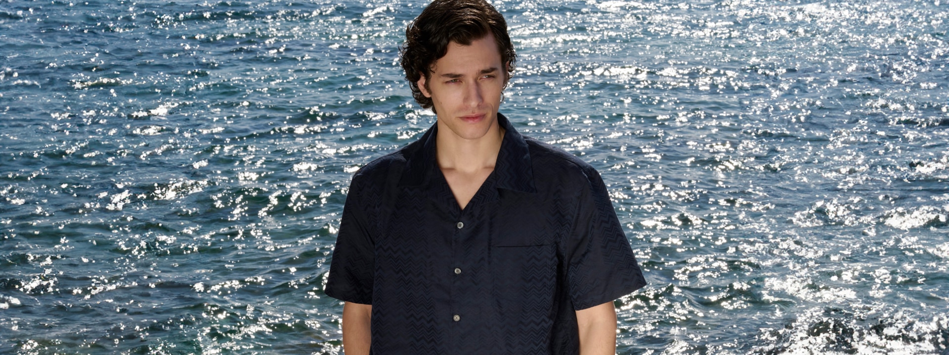 A model is wearing a blue shirt by the seaside