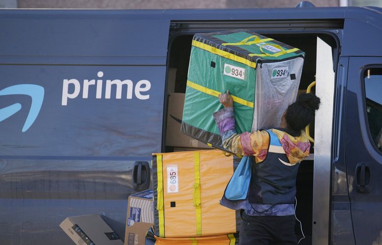 An Amazon Prime delivery person struggles with packages while making a stop at a high-rise apartment building on Nov. 28, 2023, in Denver. (AP Photo/David Zalubowski)