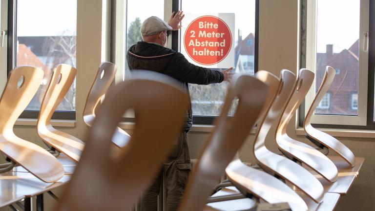 Ein Hausmeister befestigt in einem Gymnasium in Bielefeld ein Schild "Bitte 2 Meter Abstand halten" an einem Fenster.