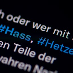 Auf dem Bildschirm eines Smartphones sieht man die Hashtags Hass und Hetze in einem Twitter-Post.