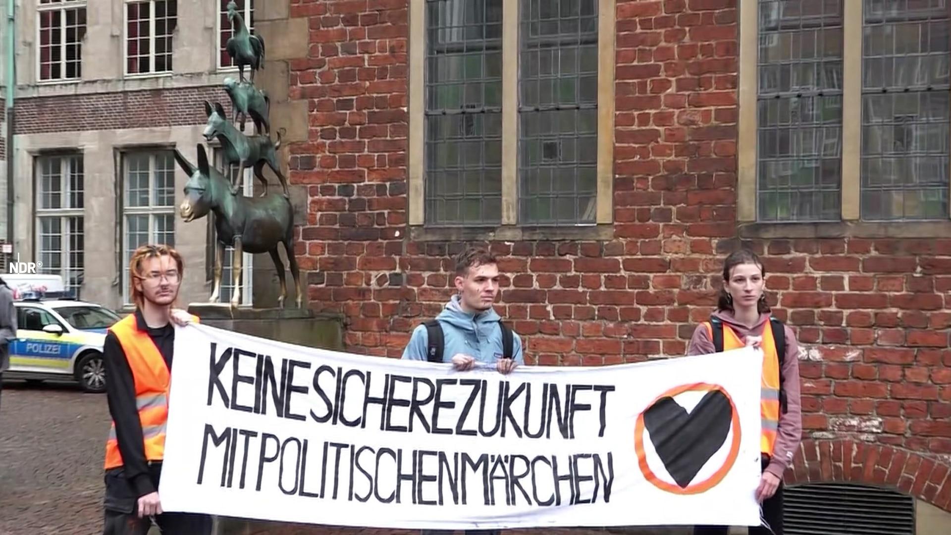 Aktivisten der "Letzte Generation" protestieren mit einem Plakat vor den Bremer Stadtmusikaten. Die Statue ist mit schwarzer Farbe beschmiert.