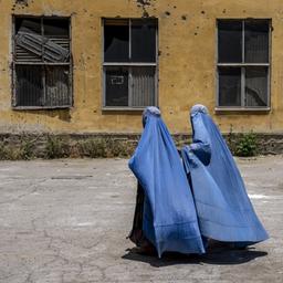 Zwei Frauen in blauer Burka laufen in Kabul an einem durch Schüsse beschädigtem Haus vorbei.