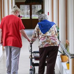 Eine Pflegerin geht mit einer Heimbewohnerin am Rollator durch den Flur eines Pflegeheims.