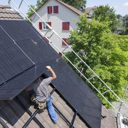 Ein Mann bei der Installation einer Solar und Photovoltankikanlage auf dem Dach eines Einfamilienhaus 