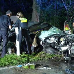 Ein komplett zertrümmertes Auto steht neben der Straße, davor stehen zwei Polizisten.