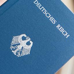 Ein Mann hält ein Heft mit dem Aufdruck "Deutsches Reich Reisepass" in der Hand.