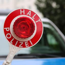 Ein Polizist hält eine Polizeikelle vor einem Streifenwagen.