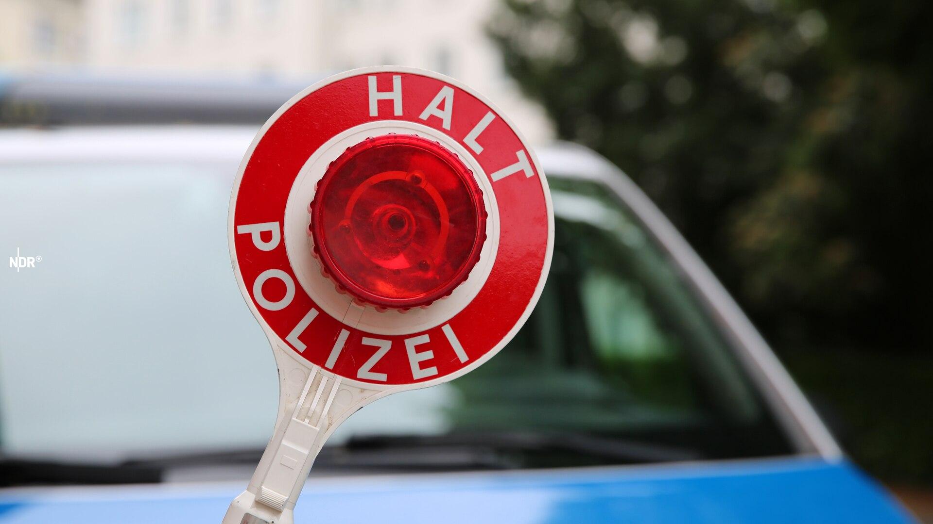 Ein Polizist hält eine Polizeikelle vor einem Streifenwagen.