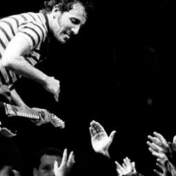 Bruce Springsteen spielt Gitarre auf einer Bühne - Hände ragen aus dem Zuschauerraum hervor. Transparenzhinweis: Das Foto stammt von einem Konzert in New Jersey, 1981.
