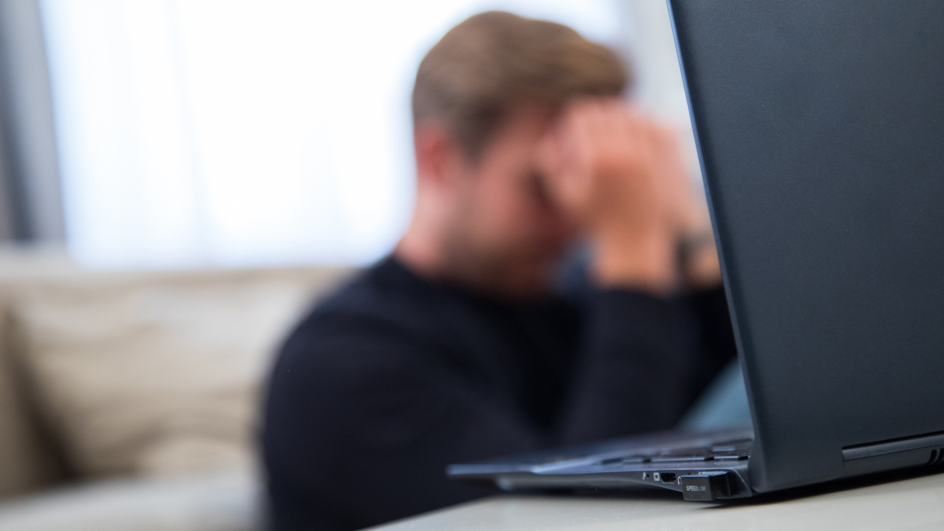 Ein Mann sitzt vor einem Laptop und fasst sich an den Kopf. 