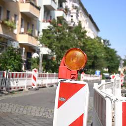 Rot-weisse Baustellenbegrenzungen sperren die Parkplätze entlang einer Straße ab, im Vordergrund steht eine orangene Warnlampe.