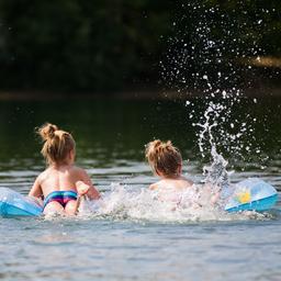 Kinder baden mit Luftmatratze in einem See.