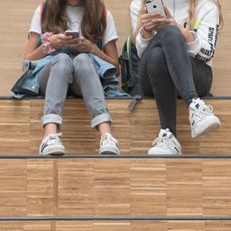 Zwei Mädchen sitzen auf einer Treppe und blicken auf ihre Smartphones.