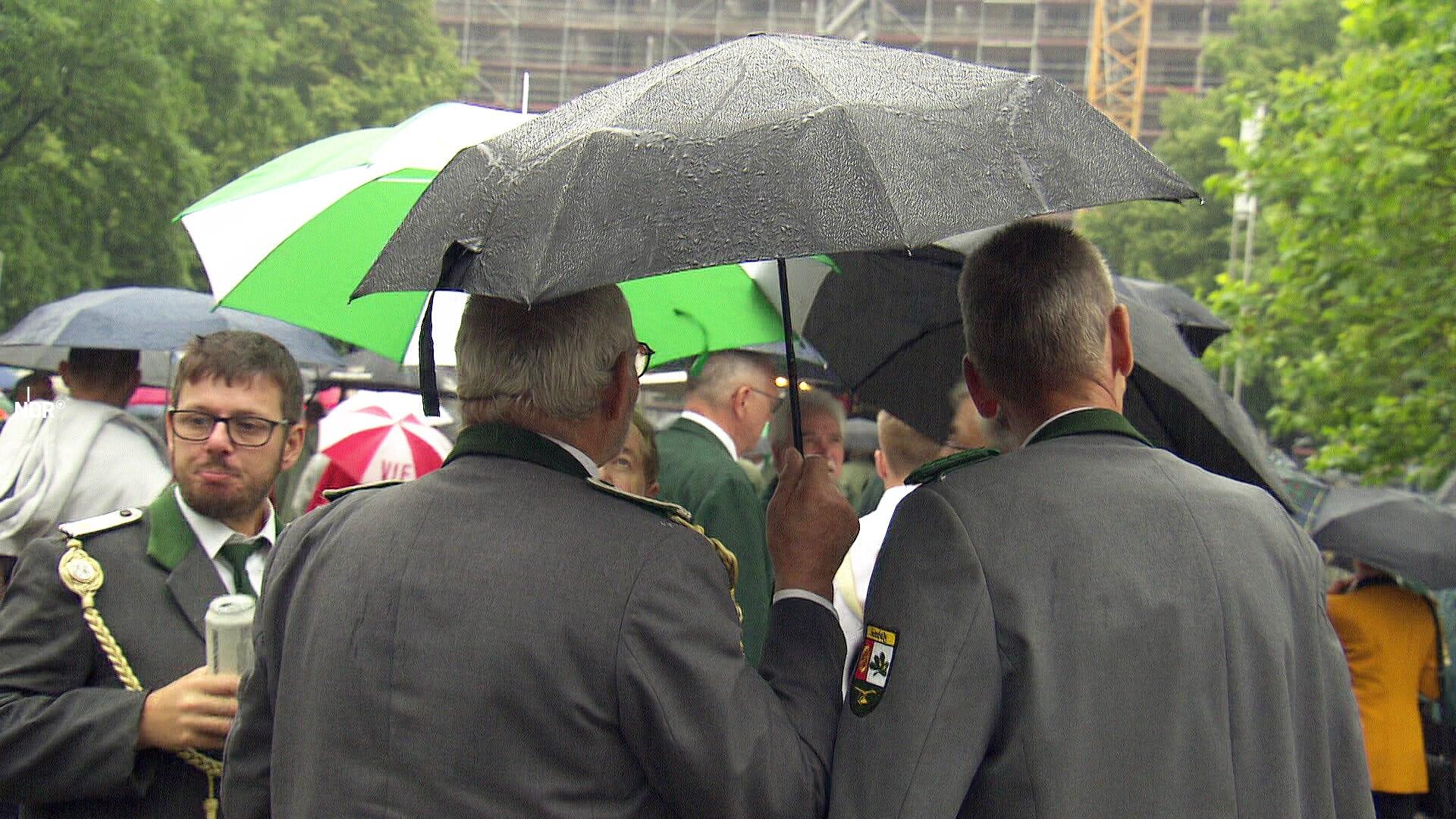 Teilnehmer des Schützenausmarsches in Hannover stehen unter einem Regenschirm.